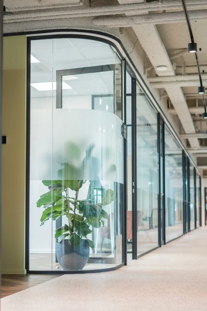 Moderne kantoorruimte aan de Joop Geesinkweg met glazen wanden en een grote groene plant in een glazen hoekkamer.